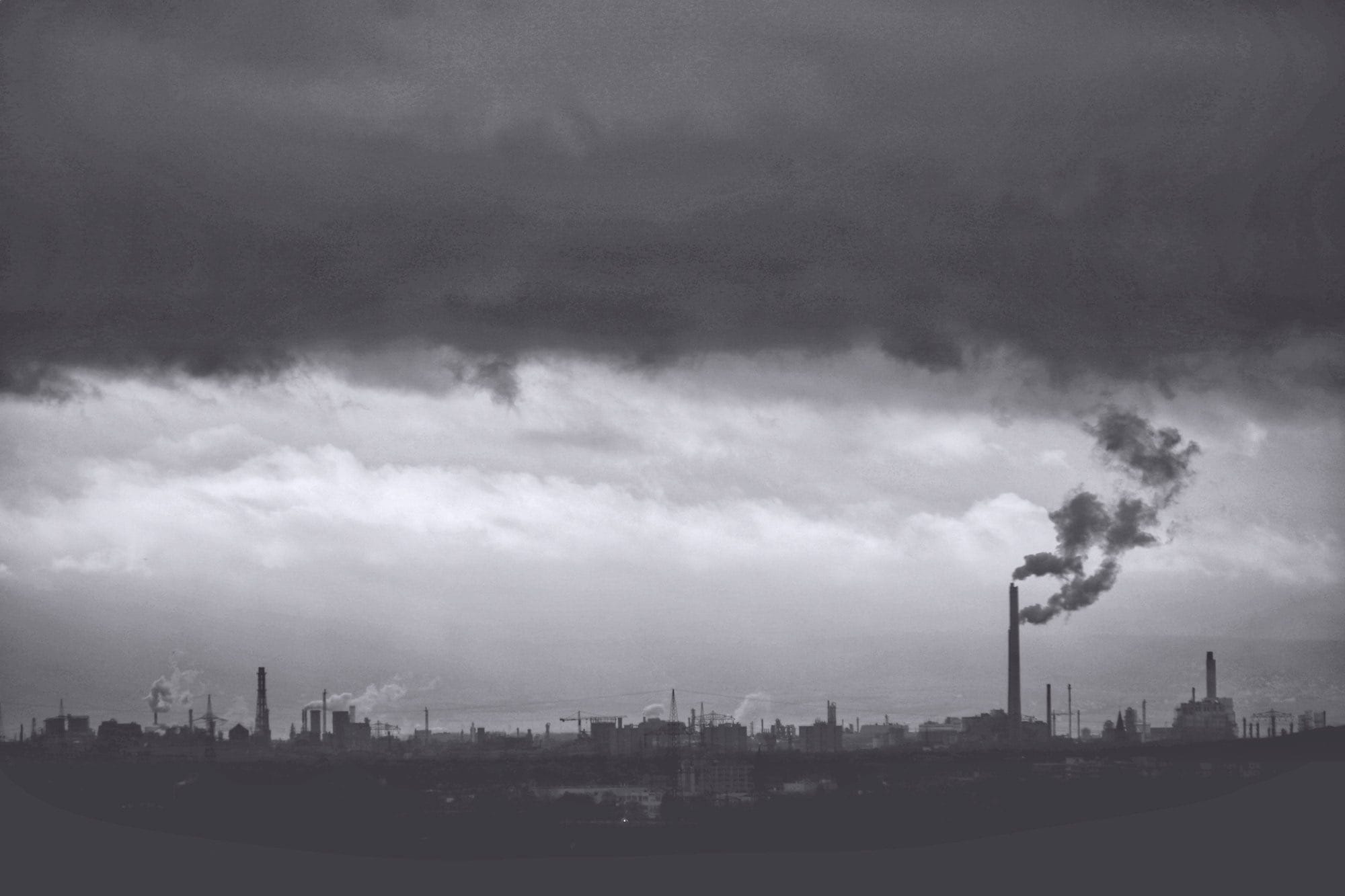 a black and white photo of a factory with smoke coming out of it